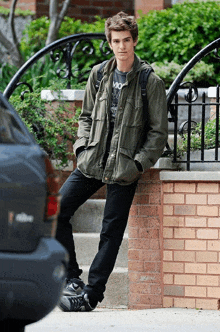 a young man leaning against a brick wall with his hands in his pocket