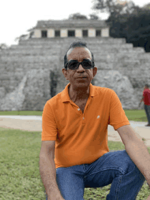 a man wearing sunglasses and an orange shirt is kneeling down