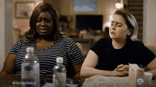 two women are sitting at a table with bottles of water and a box of popcorn with nbc written on it