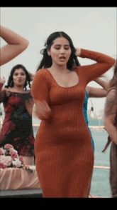 a woman in an orange dress is dancing in front of a group of other women