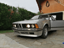 a silver bmw with its doors open is parked in front of a wooden garage