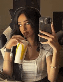 a woman is taking a selfie with her cell phone while drinking a mcdonald 's cup .