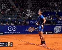 a man is holding a tennis racquet on a tennis court in front of a sign that says visit argentina