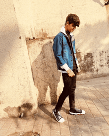 a young man wearing a denim jacket and black jeans is walking down the street