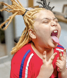 a young boy with dreadlocks and a red shirt making a funny face