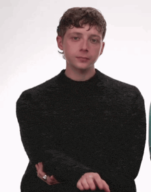 a young man wearing a black sweater with a silver ring on his finger