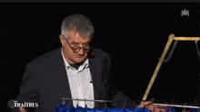 a man in a suit and glasses stands in front of a curtain that says les traitres