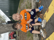 two young boys are sitting next to each other with one wearing an orange shirt that says " i am the best "