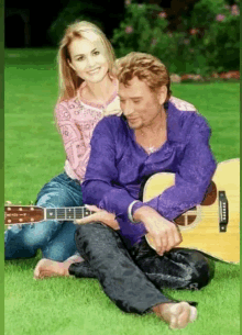 a man in a purple shirt sits on the grass with a woman holding a guitar