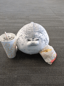 a stuffed seal sitting next to a bag of french fries and a mcdonald 's cup