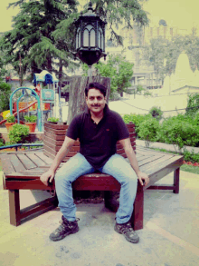 a man in a black shirt is sitting on a wooden bench in a park