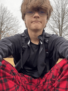 a young boy wearing glasses and a black jacket is sitting on the ground