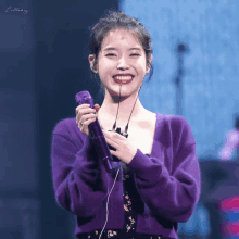 a woman in a purple sweater smiles while holding a microphone