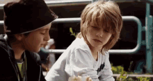 two young boys are sitting next to each other looking at something . one of the boys is wearing a hat .