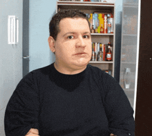 a man wearing a black shirt is sitting in front of a bookshelf with a box of hot sauce on it