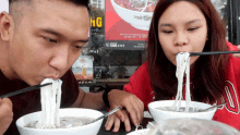 a man and a woman are eating noodles with chopsticks in front of a sign that says " ung "