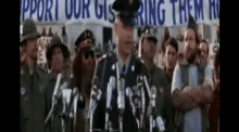 a man in a military uniform is giving a speech in front of a crowd with a sign that says support our gis