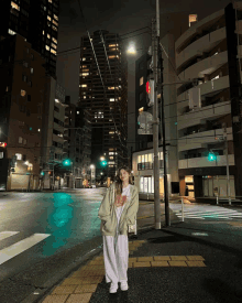 a woman in a white t-shirt stands on a city street at night