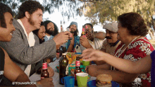 a group of people are sitting around a table with bottles of beer and a nbc logo in the corner