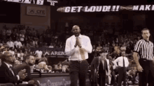 a man is standing on a basketball court in front of a crowd while a referee stands behind him .