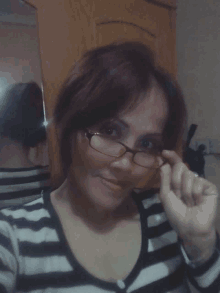 a woman wearing glasses and a striped shirt is taking a selfie