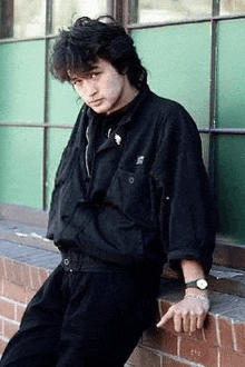 a young man is leaning against a brick wall .