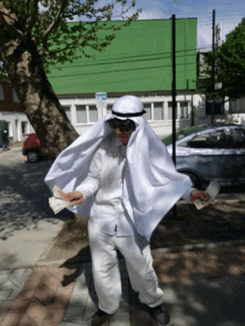 a man in a white cape is standing on a sidewalk in front of a green building with a parking sign