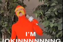 a man in an orange suit is holding a microphone and says i 'm jokinnnnnng