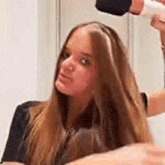a woman is blow drying her hair with a blow dryer in front of a mirror .