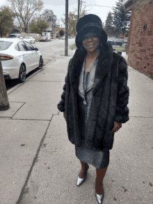 a woman wearing a fur coat and hat stands on the sidewalk