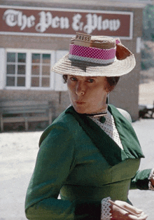 a woman in a green dress and hat stands in front of a building that says the pen & plow