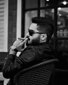 a man with a beard and sunglasses is sitting in a chair and smoking a cigarette .