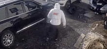 a man wearing a white nike sweatshirt is standing in front of a black suv .