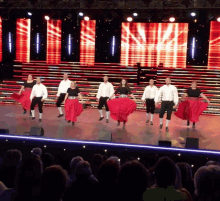 a group of people are dancing on a stage with a large screen behind them that says ' i love you '