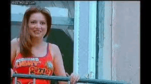 a woman in a red tank top is standing on a balcony looking out a window .