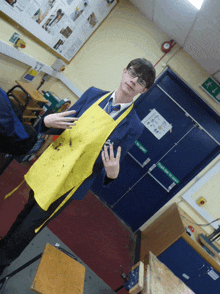 a man wearing a yellow apron stands in front of a green door that says push here for emergency