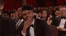 a man in a tuxedo and bow tie is sitting in a crowd of people at an awards show .