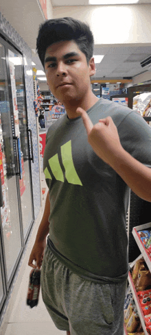 a young man wearing a grey adidas shirt is pointing to his chest