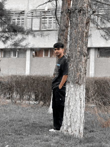 a young man leaning against a tree wearing a black shirt that says ' snoop dogg ' on it