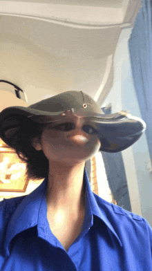 a woman wearing a blue shirt and a hat looks like she is making a funny face