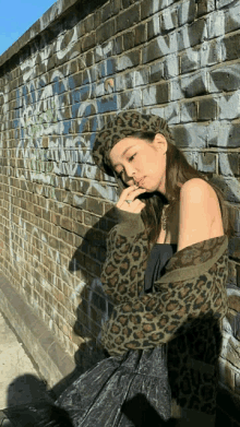 a woman leaning against a brick wall wearing a leopard print sweater