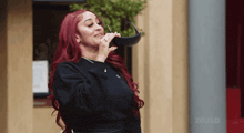 a woman with red hair holds a pair of sunglasses in her mouth