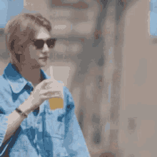 a man in a denim jacket and sunglasses is drinking a drink through a straw .