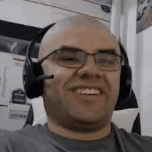 a bald man wearing headphones and glasses is smiling .