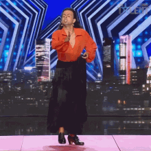 a man in a red shirt and black skirt is dancing on a stage in front of a sign that says " greatest talent "