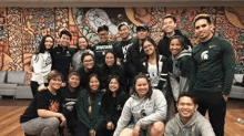 a group of young people are posing for a picture together in front of a mural .