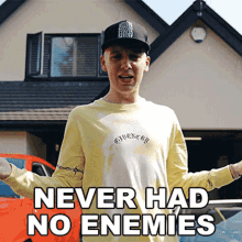 a man wearing a yellow shirt and a black hat is standing in front of a house that says never had no enemies