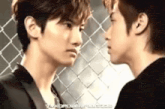 two men are standing next to each other in front of a chain link fence .