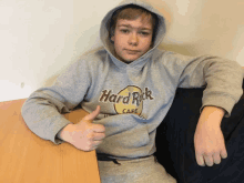 a young boy wearing a grey hard rock cafe hoodie gives a thumbs up