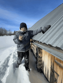a boy in a gray jacket and black hat is standing in the snow near a metal roof